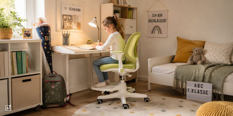 Ein Erstklässler-Kind sitzt auf einem Kinderschreibtischstuhl am Schreibtisch und macht Hausaufgaben