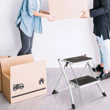Weiße Klappleiter SOLID W1 mit zwei schwarzen Stufen neben einem Umzugskarton von hjh OFFICE